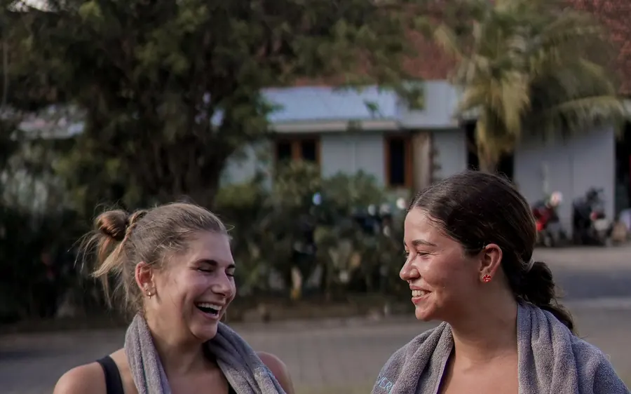 Duas amigas rindo depois do treino, com toalha no pescoço