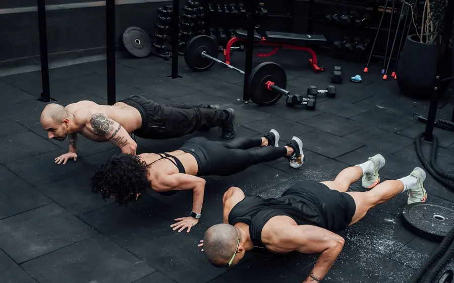 Três pessoas fazendo flexão numa academia ao ar livre