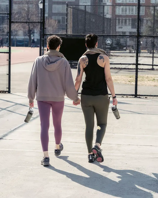 Duas mulheres de mãos dadas caminhando para a pista, com garrafas de água