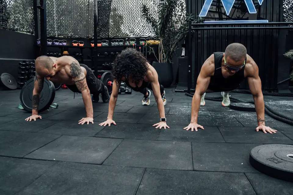 Três pessoas fazendo flexão lado a lado numa academia