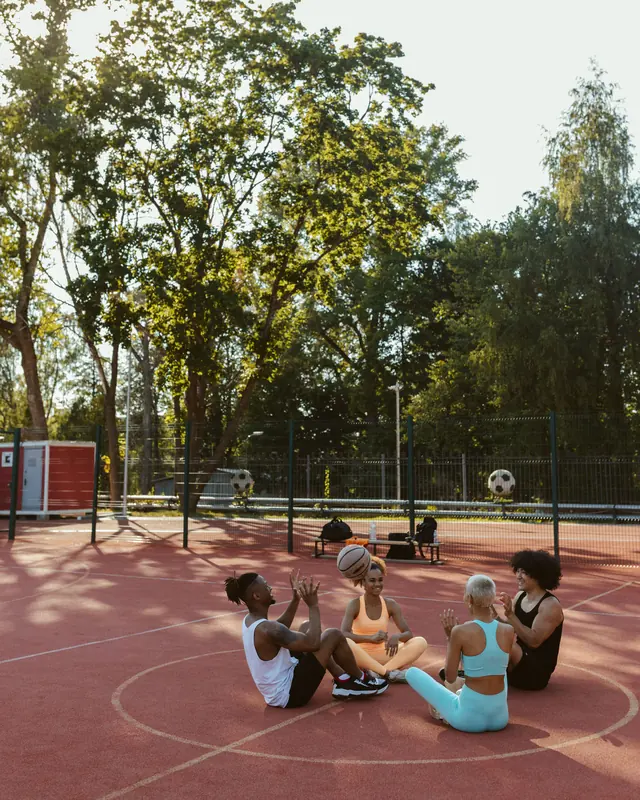 Amigos sentados numa quadra ao ar livre, jogando a bola entre si